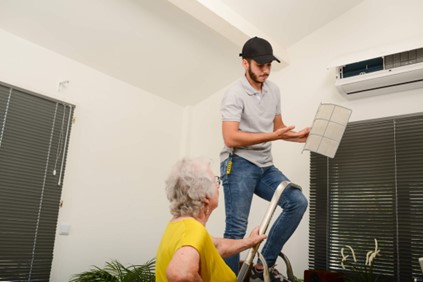 A person standing on a ladder showing an older woman the air conditioning filter 